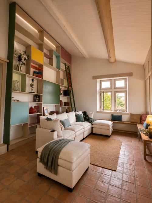 Salon moderne de l'Entre Ciel et Lettres avec canapé crème, étagères colorées, poutres en bois et grandes fenêtres