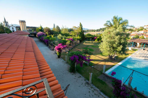 Telhado da Quinta da Malaposta com telhas de barro, buganvílias roxas, piscina e paisagem de Vila Nova de Cerveira.