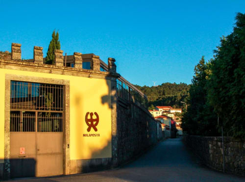 Entrada do Boutique Hotel Quinta da Malaposta com edifício de pedra amarela e logo vermelho, Vila Nova de Cerveira