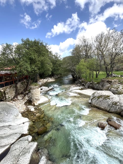 Crystal-clear mountain stream flowing through Navalguijo with lush trees and stone buildings at Casa Baelo Claudia villa