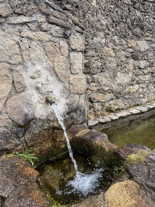 Water fountain flowing from ancient stone wall at Casa Baelo Claudia rural villa in Navalguijo, Spain