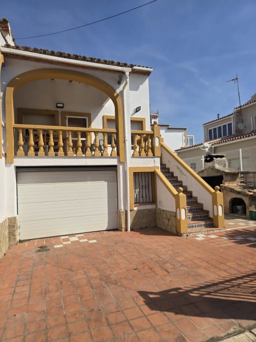 Casita amarilla y blanca con garaje en Oliva, Gandía, patio de barro y entrada cubierta con arco y balcón