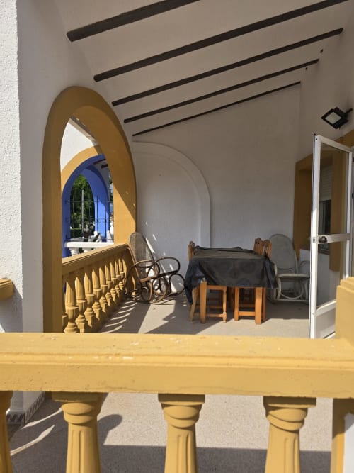 Terraza soleada con barandillas amarillas con vistas al comedor y puerta arqueada en la casa vacacional Ona en Gandía