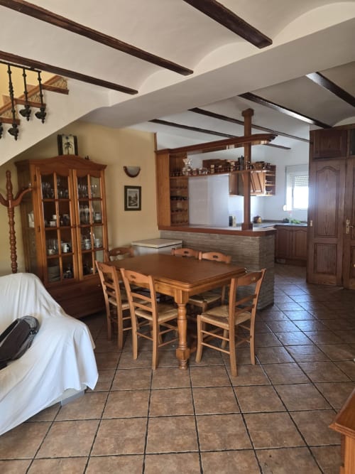 Espacioso comedor de cabaña en Oliva con mesa de madera, vigas rústicas, cocina y muebles tradicionales