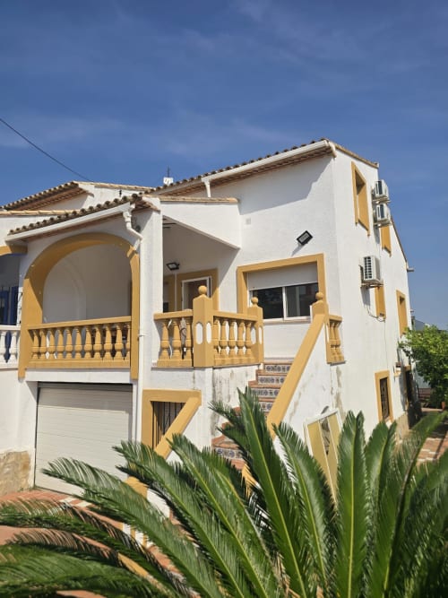 Cottage blanco y amarillo en Oliva, Gandía con terraza, garaje y plantas tropicales bajo cielo azul
