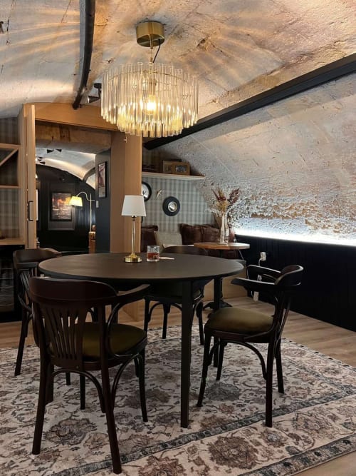 Modern dining area with round black table, bentwood chairs, crystal chandelier, and exposed stone ceiling in Bordeaux
