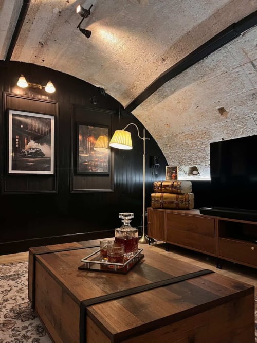 Luxurious Bordeaux apartment lounge with black paneled walls, wooden furniture, vintage suitcases, and arched stone ceiling