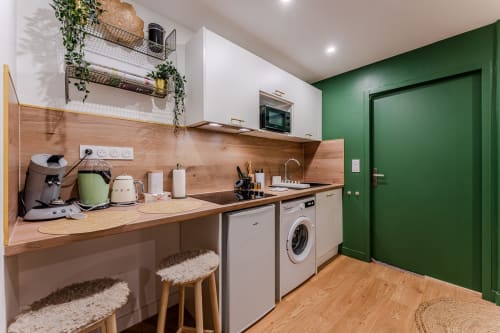 Modern kitchenette at Wellkhome Appartements in Bordeaux with wooden counters, green accent wall, and white appliances