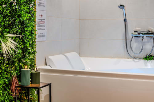 Modern bathtub with white pillows at Wellkhome Apartments in Bordeaux, featuring green living wall and rainfall shower