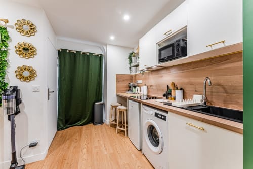 Modern kitchen in Wellkhome Bordeaux apartment with wood backsplash, white cabinets, and green accents