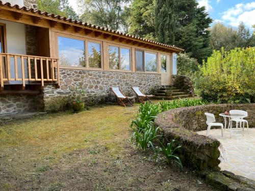 Vista do jardim Casa do Plátano na Quinta da Mata de Baixo, Portugal, com chalé de pedra, espreguiçadeiras e zona de estar