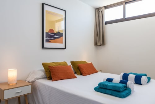 Bright bedroom with sea view artwork, colorful pillows, rolled towels, and modern furnishings at Home Stay Gran Canaria