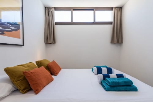 Modern bedroom in Cactus Dunes Seaview apartment, Gran Canaria, with white bed, colorful pillows, towels, and sea view