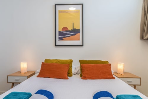 Modern bedroom with sunset-themed coastal artwork, orange pillows, twin bedside lamps, sea view at Cactus Dunes Seaview