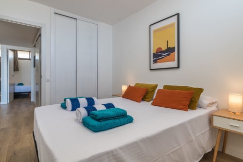 Modern bedroom with sea view at Home Stay Gran Canaria, featuring queen bed with colorful cushions and folded towels