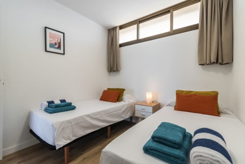 Twin beds with colorful pillows and towels in bright apartment bedroom with sea view windows at Home Stay Gran Canaria