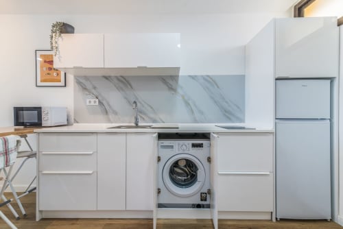 Modern kitchen in Gran Canaria apartment with white cabinetry, marble backsplash, integrated washing machine, and stainless