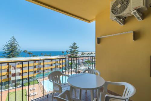 Balcony terrace with sea view, white chairs, table, air conditioning unit, and beach resort buildings in San Bartolomé de