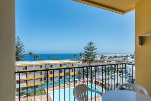 Balcony view of swimming pool, gardens, and Mediterranean Sea at Cactus Dunes apartment, Gran Canaria
