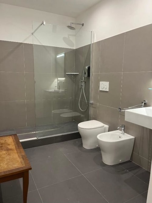 Bagno moderno a Domus Giovanna Roma con cabina doccia in vetro, toilet e bidet bianchi, lavabo vessel e piastrelle scure