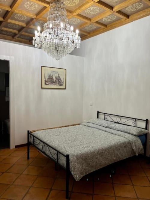 Elegante Camera Doppia Deluxe presso Domus Giovanna Roma B&B con letto in ferro battuto, lampadario di cristallo e soffitto in legno intarsiato