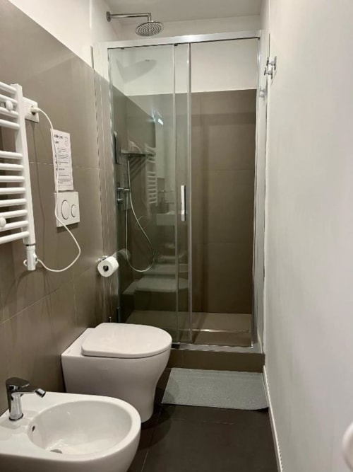 Bagno moderno a Domus Giovanna Roma con doccia in vetro, wc bianco, lavabo, scaldasalviette e pareti rivestite