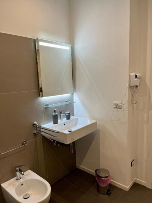 Moderno bagno presso Domus Giovanna Rome BnB con specchio illuminato, lavabo bianco, bidet e pavimento in piastrelle scure