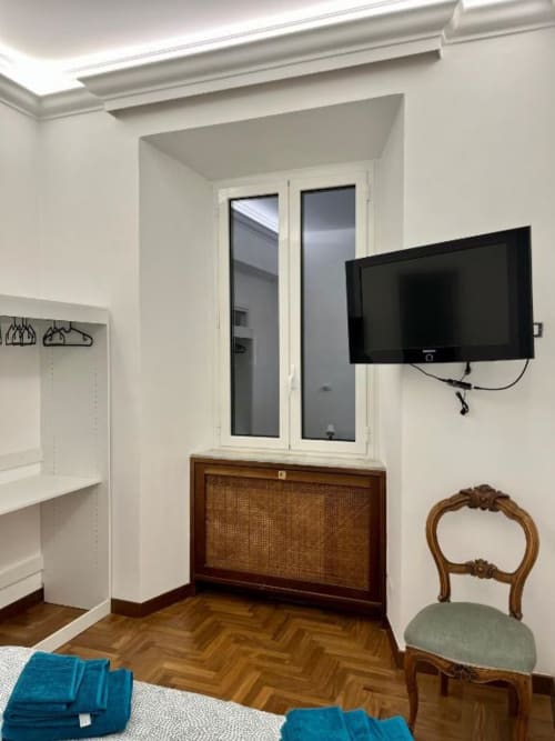 Camera luminosa e moderna a Domus Giovanna Roma con TV a parete, cassettone in legno, sedia verde e vista sulla città