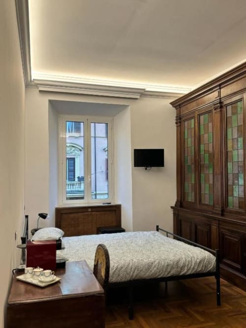 Camera elegante di Domus Giovanna Roma con letto, armadio in legno, TV e finestra con vista su monumenti