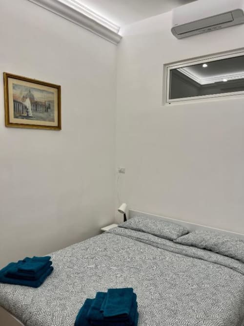 Camera moderna della Domus Giovanna Roma B&B con letto grigio, aria condizionata, finestra e quadri incorniciati su pareti bianche