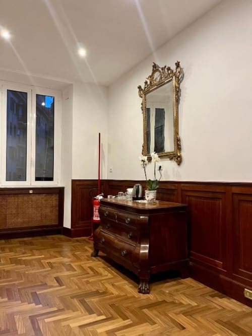 Elegante camera doppia presso Domus Giovanna a Roma con comò in legno antico, specchio dorato ornamentale, pavimentazione in legno duro e arredi scuri