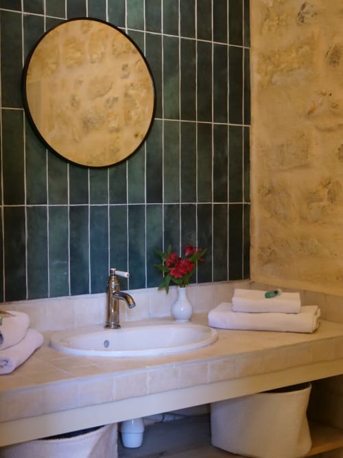Lavabo élégant du gîte Mas Petit Prince à Arles avec miroir rond, fleurs rouges et carrelage rayé