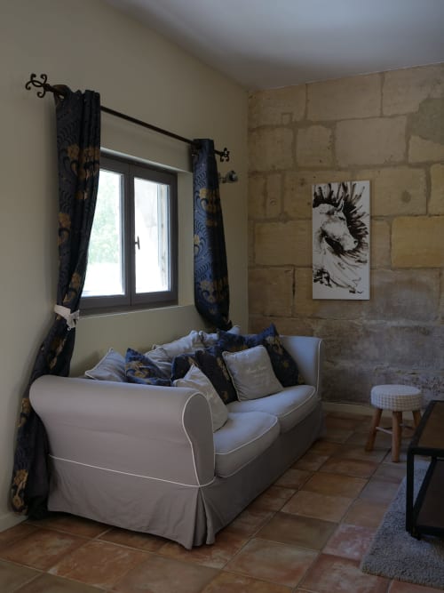 Coin salon douillet du Gîte d'Anna au Mas Petit Prince, Arles avec canapé crème, rideaux à motifs sombres et fenêtre vue jardin