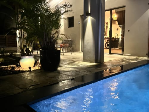 Piscine privée illuminée la nuit avec terrasse, plantes tropicales et espace de vie en plein air aux Hébergements Passion
