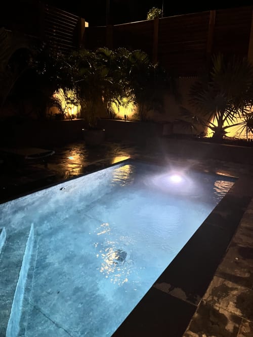 Piscine privée illuminée la nuit avec végétation tropicale et clôtures en bois aux Hébergements Passion, Martinique