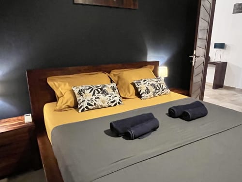 Chambre moderne avec lit en bois, parure jaune, oreillers motifs et serviettes roulées aux Hébergements Passion