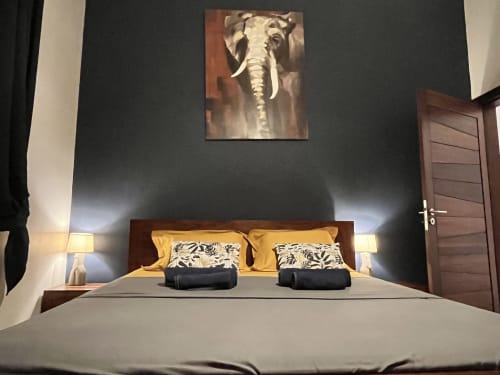 Chambre avec lit en bois, oreillers jaunes, tableau d'éléphant, appliques murales et mur d'accent foncé aux Hébergements
