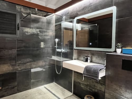 Salle de bain moderne avec carrelage sombre, cabine de douche vitrée et miroir lumineux au gîte Les Hébergements Passion