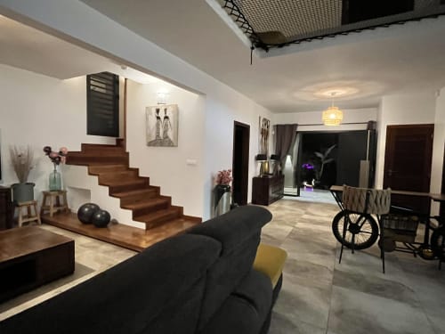 Séjour ouvert avec escalier en bois, canapé noir, salle à manger et vélo aux Hébergements Passion