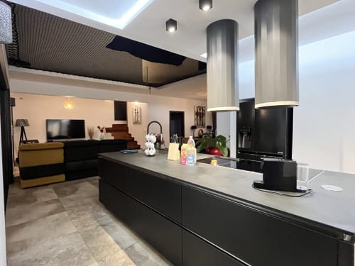 Cuisine moderne avec îlot aux plans de travail noirs, hotte aspirante en acier inoxydable, et espace ouvert dans Hébergement Passion