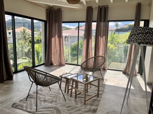 Salon moderne avec fauteuils en rotin, vues panoramiques sur les montagnes et la verdure de la Martinique aux Hébergements Passion