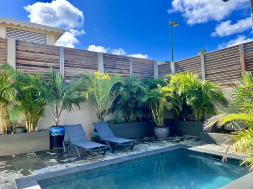 Piscine privée et espace détente aux Hébergements Passion en Martinique, avec plantes tropicales et clôture bois