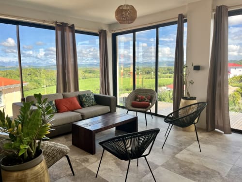 Salon moderne du gîte Les Hébergements Passion avec vue panoramique sur la vallée, canapé gris, fauteuils en osier et verdure