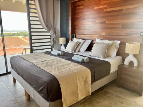 Chambre moderne aux Hébergements Passion en Martinique avec vue mer, mur en bois, literie beige et balcon