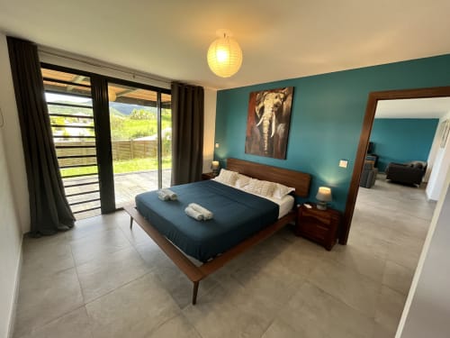 Chambre moderne avec mur d'accent turquoise, lit en bois, literie bleu foncé, portes vitrées sur terrasse, œuvre d'éléphant