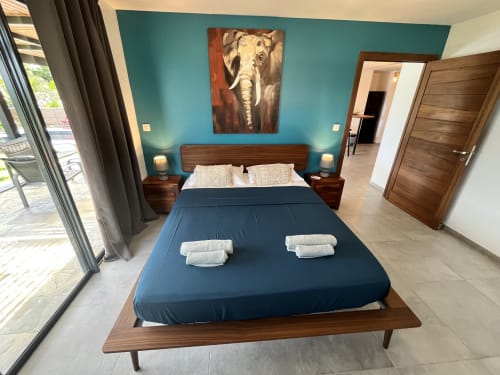 Chambre moderne aux Hébergements Passion avec mur turquoise, lit en bois, tableau d'éléphant et vue sur mer
