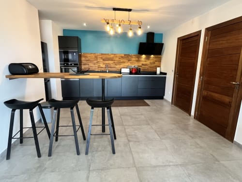Cuisine moderne et bar avec comptoir en bois, armoires noires et places assises au gîte Passion Vanille Cannelle