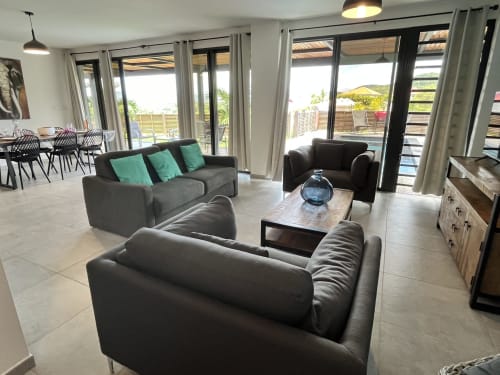 Salon moderne avec canapés gris, vue sur mer par portes vitrées et coin repas du gîte Les Hébergements Passion