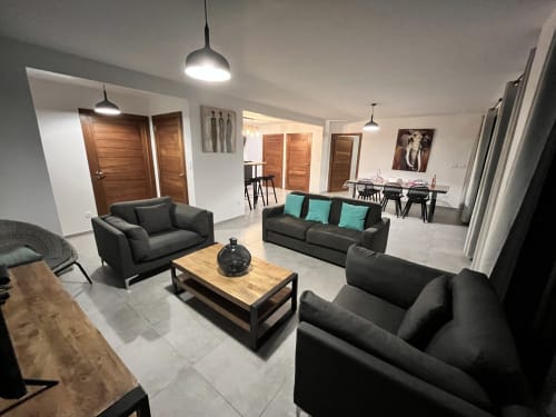 Salon moderne du gîte Les Hébergements Passion en Martinique avec canapés noirs, table en bois et coin repas