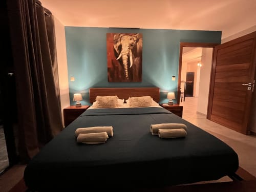 Chambre élégante aux murs bleu acier, mobilier en bois, œuvre d'éléphant et literie noire aux Hébergements Passion